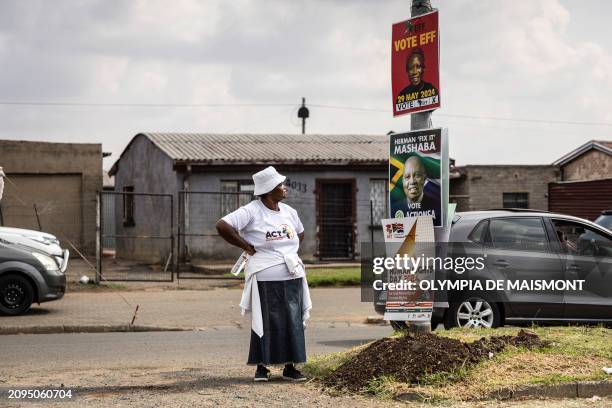 Woman wearing a shirt of African Congress for Transformation party looks at other parties' election posters on a pole in Sharpeville, on March 21,...