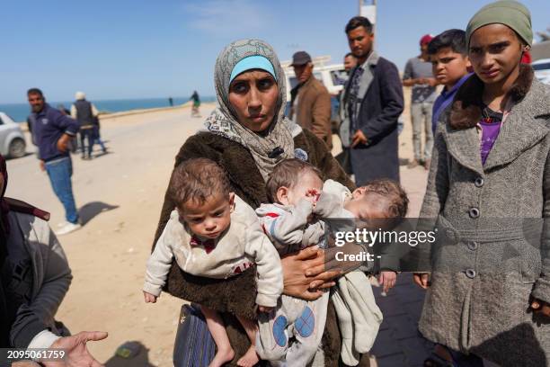 Woman carries three babies as she reaches the central part of the Gaza Strip after fleeing the Al-Shifa hospital compound in Gaza City, on March 21,...