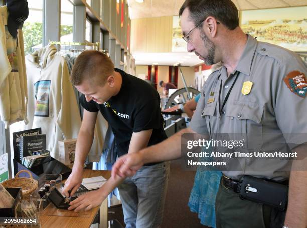 Mikah Meyer, left, gets some help from NPS acting chief of interpretion William Valosin as he adds a National Park Passport Stamp for Saratoga...