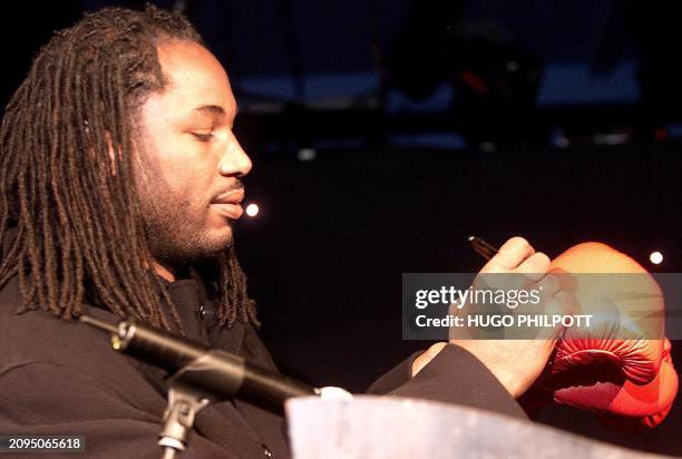 British boxer Lennox Lewis signs a boxing glove as he and American colleague Muhamed Ali launch a new Playstation game called "Knockout Kings" in...