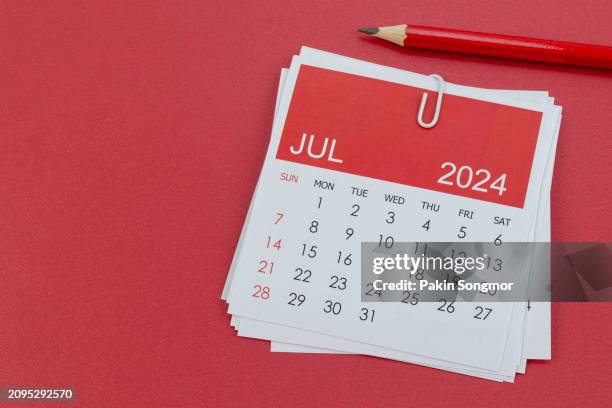 desk calendar 2024: july calendar is used to plan daily work and life with red pencil on a red paper background. - julio fotografías e imágenes de stock