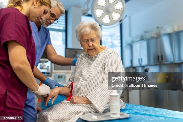 nurse and doctor preparing elderly patient for surgery, inserting iv cannula in her hand. - inserting iv stock pictures, royalty-free photos & images