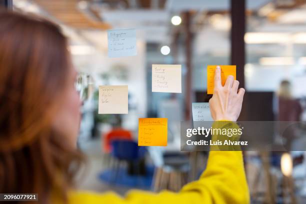 businesswoman brainstorming putting sticky notes on a glass screen during brainstorming session in office - collant description physique photos et images de collection