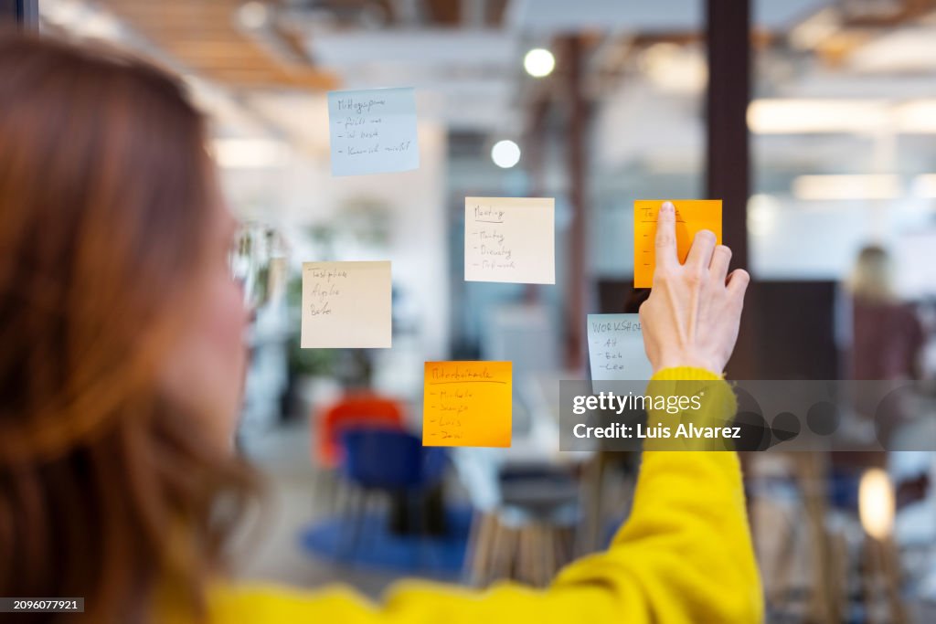 Businesswoman brainstorming putting sticky notes on a glass screen during brainstorming session in office