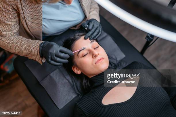 female beautician microblading her client's eyebrows at a beauty salon - female body waxing stock pictures, royalty-free photos & images