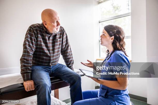 nurse and senior man discussing treatment in exam room - examination table stock pictures, royalty-free photos & images