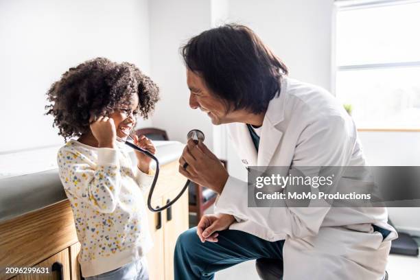 young girl and doctor playing with stethoscope - pediatra fotografías e imágenes de stock
