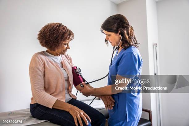 nurse checking senior woman's blood pressure in exam room - indicador de presión sanguínea fotografías e imágenes de stock