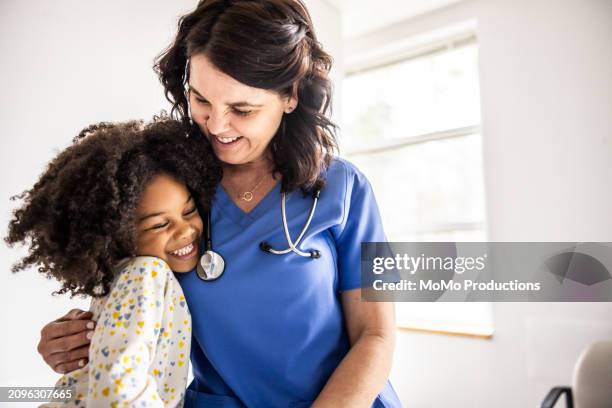 young girl embracing nurse in doctors office - suivi des malades photos et images de collection