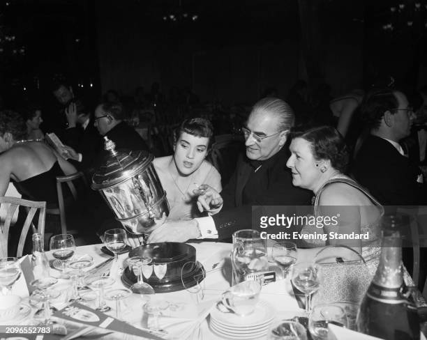 Rally driver Pat Moss looks at a silver trophy with her father, former racing driver Alfred Moss and mother Aileen Moss at the BRDC dinner, London,...