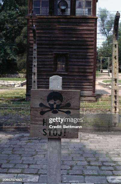 View of a sign near a guard tower in the Auschwitz concentration camp, Oświęcim, Poland, June 7th 1979. The sign depicts a skull above the word...