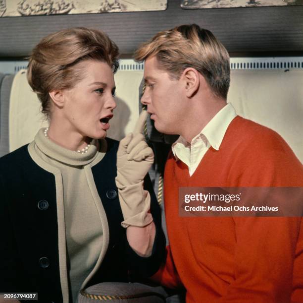 American actress Angie Dickinson, wearing a beige turtleneck sweater beneath a black round-neck jacket with beige trim and beige evening gloves, wags...