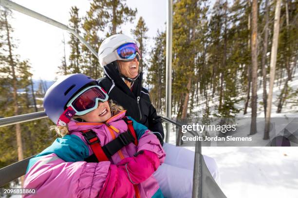 a grandmother and her granddaughter riding a chairlift while skiing together. - light vivid children senior young focus foto e immagini stock