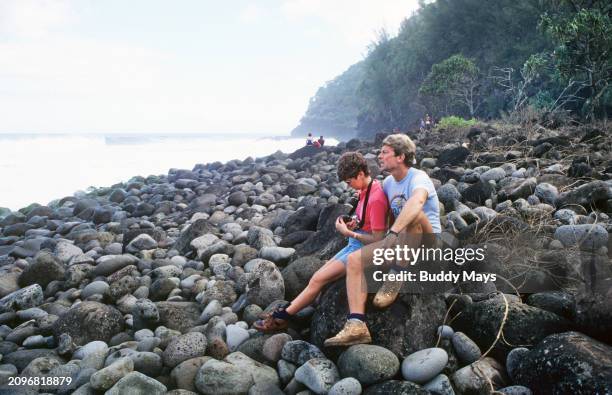 Exhausted hikers rest on a rocky beach along the Kalalau Trail on the Na Pali Coast, island of Kauai, Hawaii, 2007. .