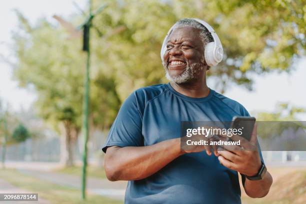 hombre mayor usando un teléfono inteligente mientras corre en un parque público - un solo hombre mayor fotografías e imágenes de stock
