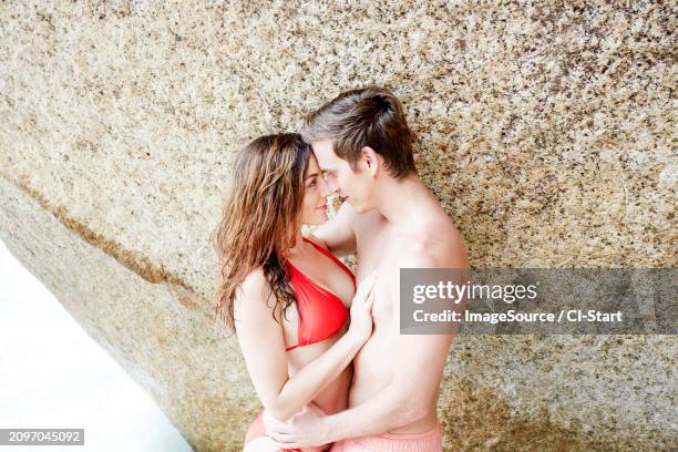 young couple embracing by boulder on beach - boulders beach stock pictures, royalty-free photos & images