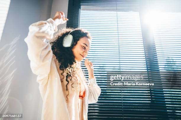 a curly girl in headphones dances near the window. - facilité photos et images de collection