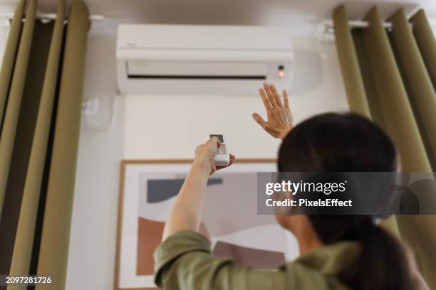 frau mit fernbedienung klimaanlage im haus - hotelzimmer stock-fotos und bilder