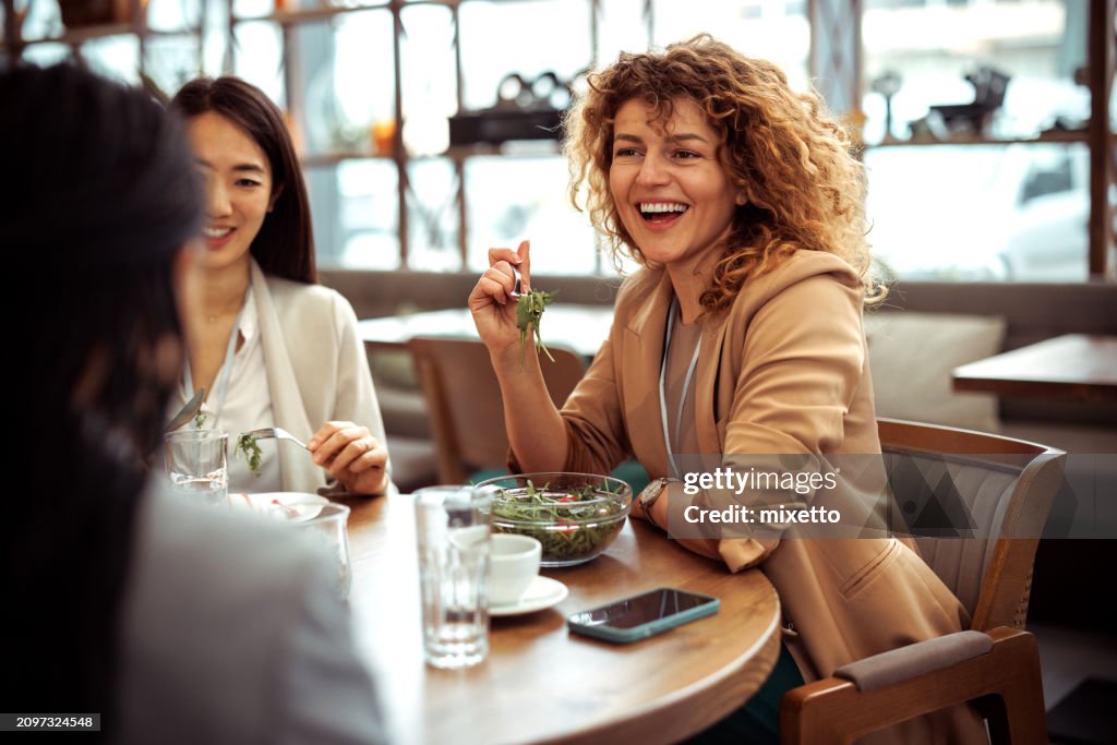 Lächelnde, gut gekleidete Geschäftsfrau, die lacht, während sie mit Kollegen im Restaurant zu Mittag isst