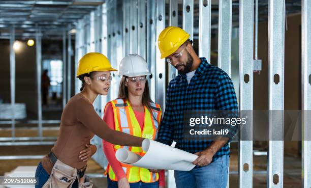 trois ouvriers de la construction sur un chantier avec des plans - regarder vers le bas photos et images de collection