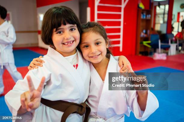 dos niños de primaria están tomando una clase de artes marciales. están de pie juntos en una fila y sonríen mientras miran a la cámara. - deporte de combate fotografías e imágenes de stock