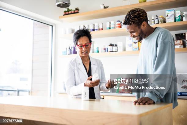 female doctor discussing supplements with young man in medical office - daily life in multicultural birmingham stock pictures, royalty-free photos & images