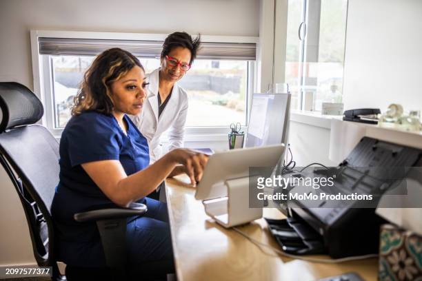 female doctor and nurse conferring at reception desk in doctor's office - reportage hospital stock pictures, royalty-free photos & images