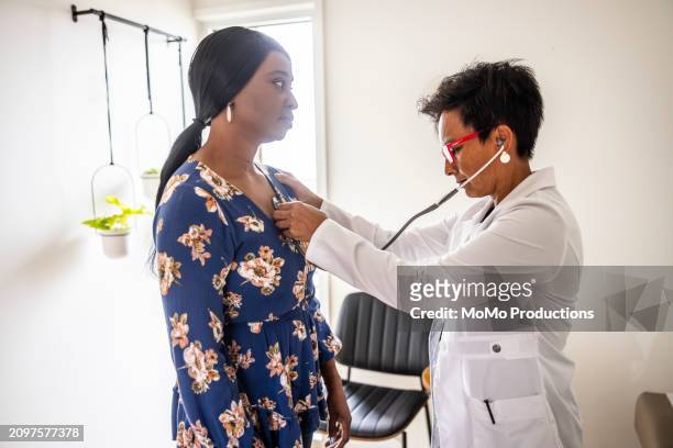 doctor listening to womans heart with stethoscope - reportage hospital stock pictures, royalty-free photos & images