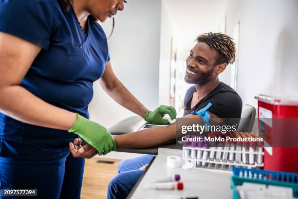 female nurse drawing blood sample from young man in medical office - bluttest stock-fotos und bilder