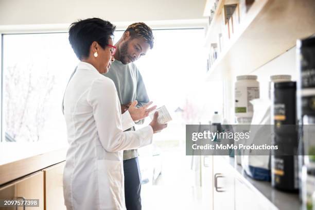 female doctor discussing supplements with young man in medical office - daily life in multicultural birmingham stock pictures, royalty-free photos & images