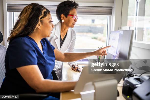 female doctor and nurse conferring at reception desk in doctor's office - reportage hospital stock pictures, royalty-free photos & images