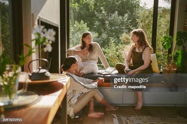 smiling female friends talking together by a window during a wellness retreat - amizade imagens e fotografias de stock