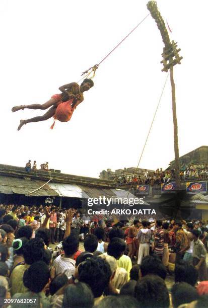 Man throws holy water from the Ganges river and consecrated fruit to devotees below while revolving from a bamboo pole in one of the rituals of...