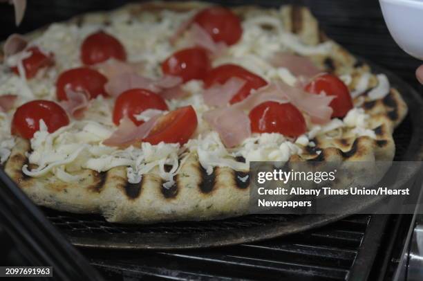 Garlic and herb pizza dough with cherry tomatoes, three cheeses and prosciutto cooks on a pizza screen on a grill at DeFazio's Pizza on Thursday,...