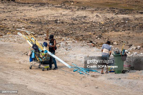 Male waste picker is seen adding a used up broom to his cart while a female waste picker is seen checking garbage, on cleared land after the...