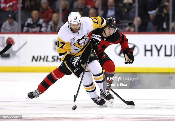 Bryan Rust of the Pittsburgh Penguins takes the puck as Luke Hughes of the New Jersey Devils defends during the first period at Prudential Center on...