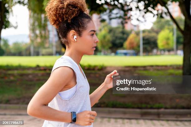 retrato lateral de una mujer corriendo al aire libre con auriculares - hispanolistic fotografías e imágenes de stock