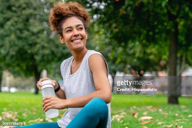 woman exercising at the park and drinking water from a bottle - hispanolistic stockfoto's en -beelden