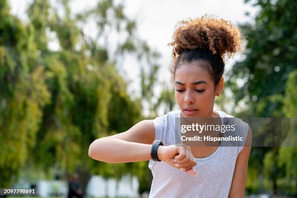 woman running outdoors and checking her fitness tracker - hispanolistic stockfoto's en -beelden