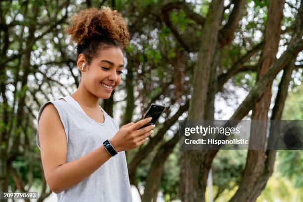 female runner listening to music on her cell phone using headphones - hispanolistic stockfoto's en -beelden