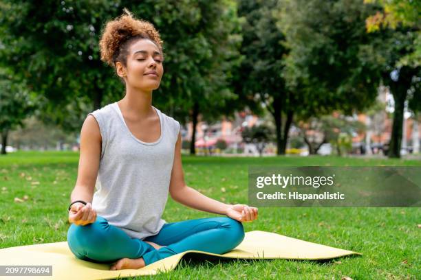 woman meditating at the park sitting on a fitness mat - hispanolistic stockfoto's en -beelden