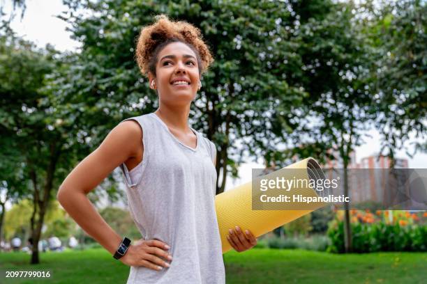 woman exercising outdoors and holding a yoga mat at the park - hispanolistic stockfoto's en -beelden