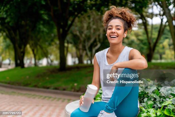 mujer en forma sonriendo en el parque mientras se toma un descanso de correr - hispanolistic fotografías e imágenes de stock