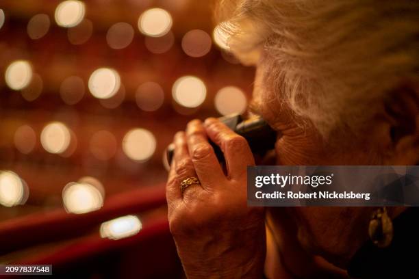 Woman focuses her binoculars on the stage of the orchestra warming for a performance of Giuseppe Verdi's "La Forza del Destino" March 12, 2024 at the...
