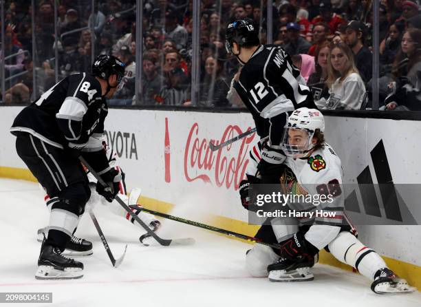 Connor Bedard of the Chicago Blackhawks loses his balance along the boards next to Trevor Moore and Vladislav Gavrikov of the Los Angeles Kings...