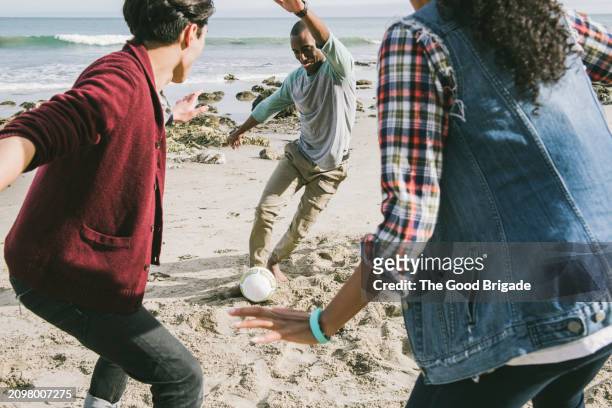 young friends playing soccer at beach on sunny day - kicking sand stock pictures, royalty-free photos & images