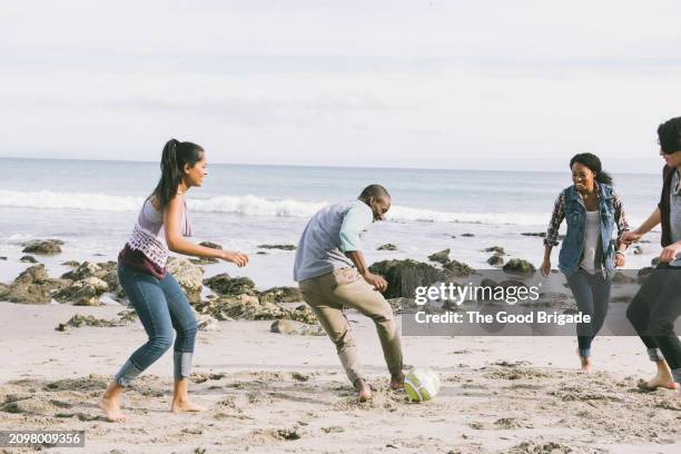 young male and female friends playing soccer at beach against sky - malibu nature stock pictures, royalty-free photos & images
