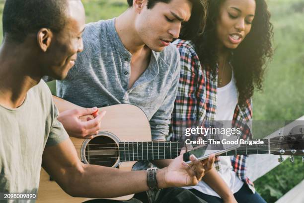 young man playing guitar with friends outdoors - acoustic guitar stock pictures, royalty-free photos & images