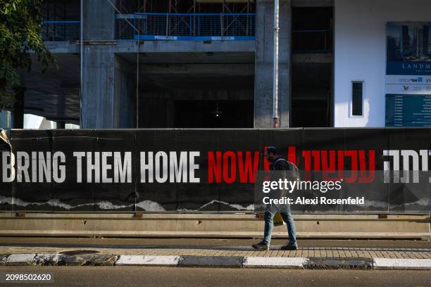 Man walks past a sign that reads "bring them home now" in English and "Now" in Hebrew on March 20, 2024 in Tel Aviv, Israel. Israeli negotiators are...