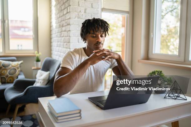 man sat at desk looking at laptop screen - opdracht om thuis te blijven stockfoto's en -beelden
